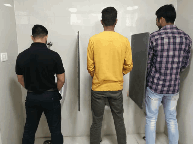 a man in a yellow shirt is urinating in a bathroom
