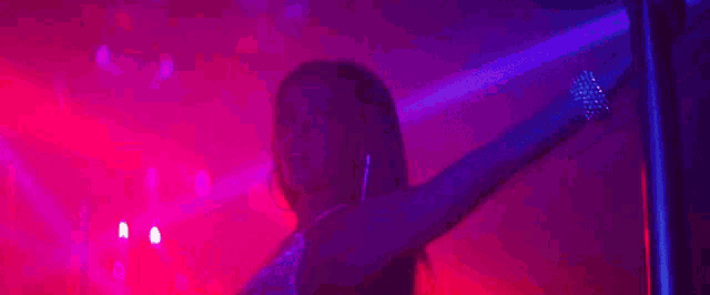 a woman is dancing on a pole in a dark room with purple and red lights .
