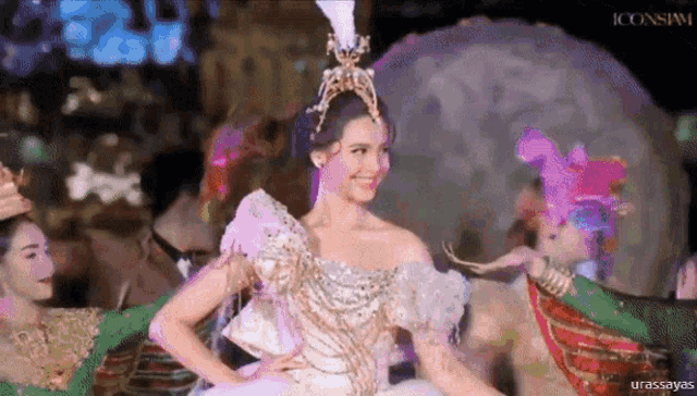 a woman in a white dress with a crown on her head is standing in front of a crowd .