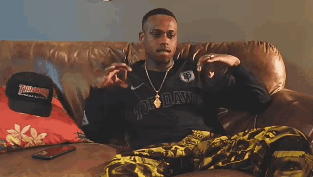 a man is sitting on a couch wearing a shirt that says thrasher