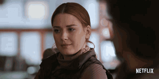 a woman with red hair is looking at a man with a netflix logo in the background