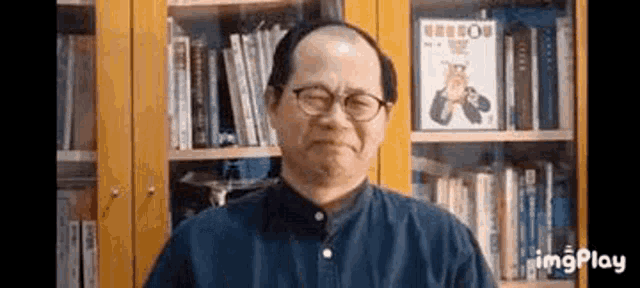 a man wearing glasses is standing in front of a bookshelf .