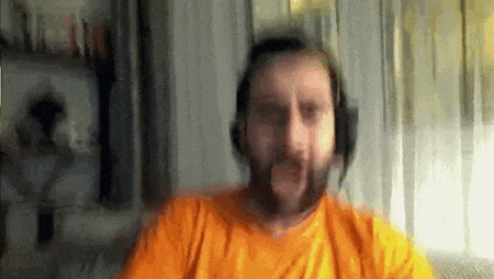 a man with a beard wearing headphones and an orange shirt is looking at the camera .