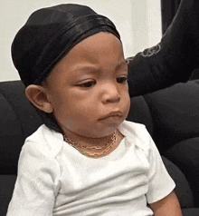 a baby wearing a white shirt and a black hat is sitting on a black couch .