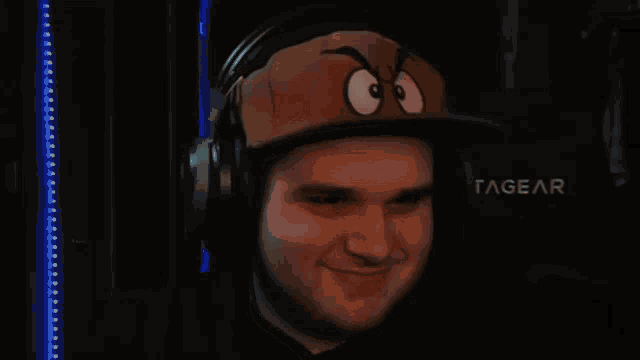 a man wearing headphones and a hat with a face on it is sitting in front of a tagear chair