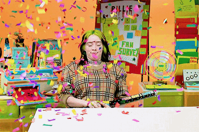 a woman is sitting at a table with confetti falling around her and a sign that says fan survey