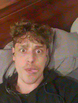 a man in a black shirt is laying on a bed making a funny face .