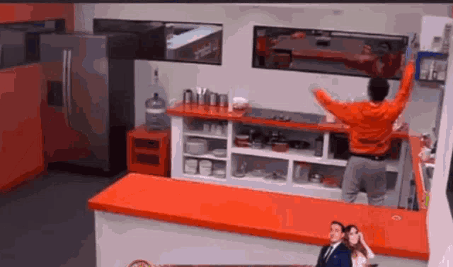 a man in a red sweater is standing in a kitchen with his arms in the air .