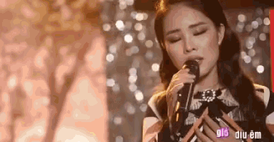 a woman is singing into a microphone with her eyes closed on a stage .