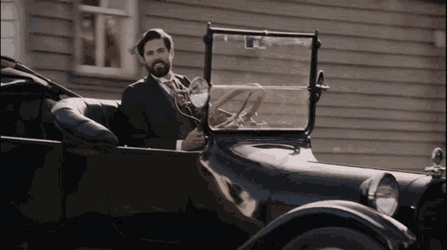 a man in a suit and tie is driving an old fashioned car
