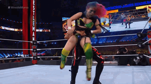 a wrestler is carrying another wrestler in a wrestling ring with a sign that says wrestlemania on it