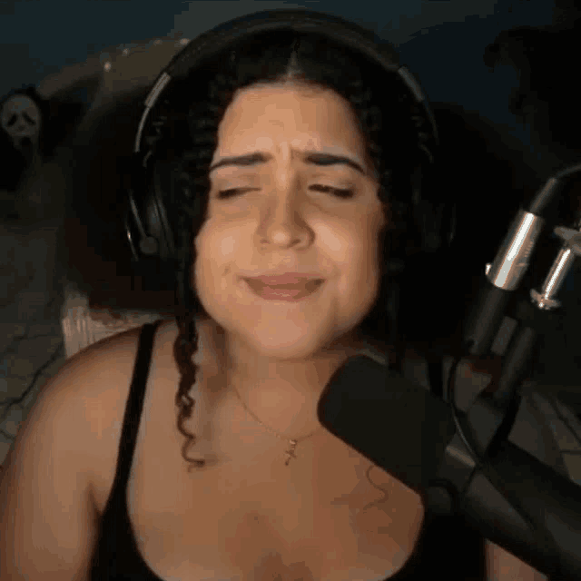 a woman wearing headphones stands in front of a microphone with her eyes closed
