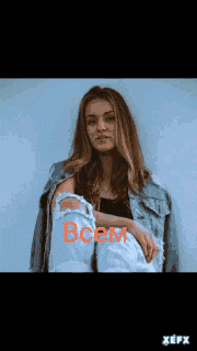 a woman in a denim jacket stands in front of a wall with the word cem written on it