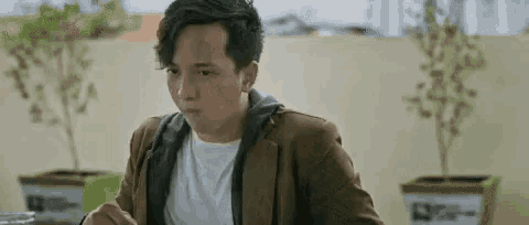 a man in a brown jacket is sitting at a table eating a meal .