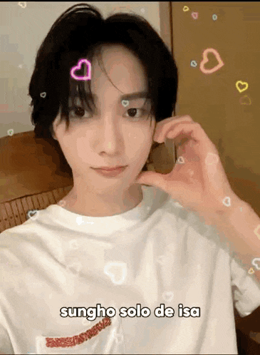 a young man is making a heart shape with his hand while wearing a white shirt .