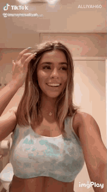 a woman in a blue tank top is smiling and looking at herself in the mirror ..
