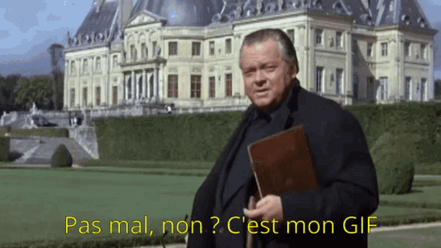 a man holding a book in front of a large building with the words pas mal non c est mon gif