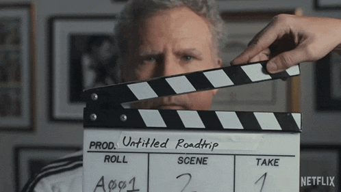 a man holding a clapper board that says " untitled roadtrip "