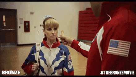 a man in a red jacket is touching a woman 's face in a scene from the bronze movie .
