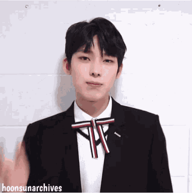 a young man in a suit and bow tie is waving his hand .