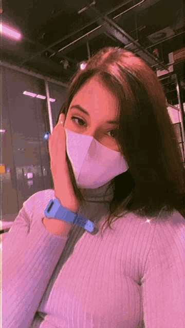 a woman wearing a purple sweater and a face mask has a blue watch around her wrist