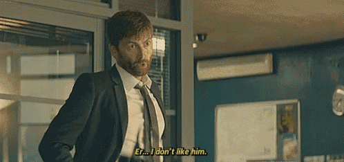 a man in a suit and tie is talking to another man in a room and says i don 't like him .