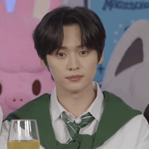 a young man wearing a green sweater and tie is sitting at a table with a glass of liquid in front of him