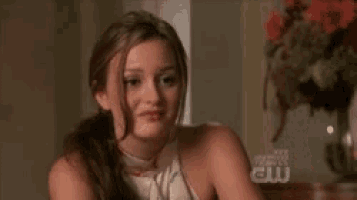 a woman is sitting at a table with a vase of flowers in the background and looking at something .