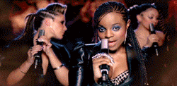 a woman singing into a microphone with another woman holding a cell phone