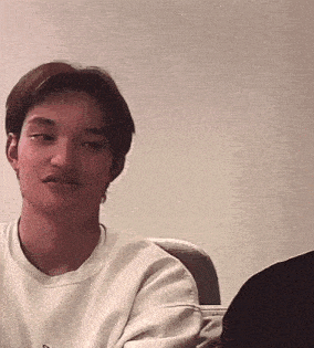 a young man with a mustache is sitting in a chair and looking at the camera .