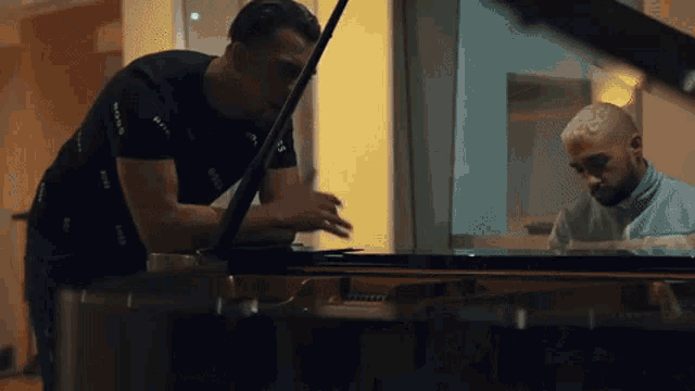 a man in a black shirt is standing next to another man playing a piano .