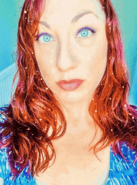 a woman with red hair and blue eyes is wearing a blue top