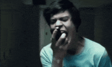 a young man in a blue shirt is standing in a dark room looking down .
