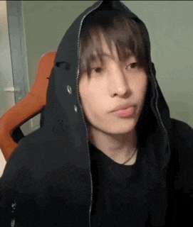 a young man wearing a black hoodie is sitting in a chair and making a face .