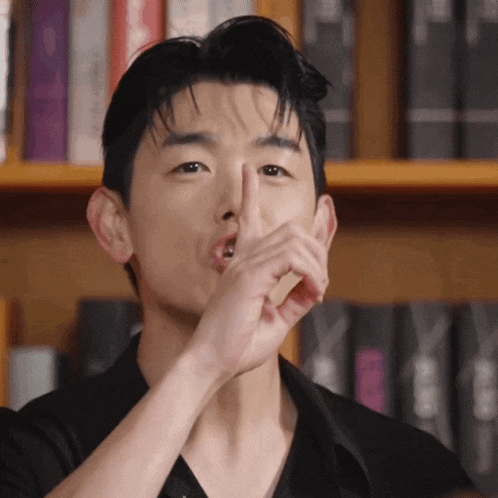 a man covering his mouth with his hand in front of a bookshelf