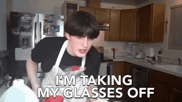 a man in an apron is taking his glasses off in a kitchen