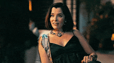 a woman in a black dress and a necklace is sitting on a chair .
