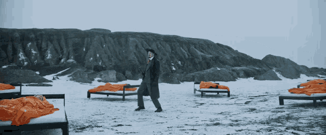 a man in a black coat is walking across a snowy beach