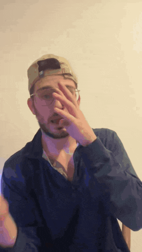 a man wearing a hat and glasses is covering his face