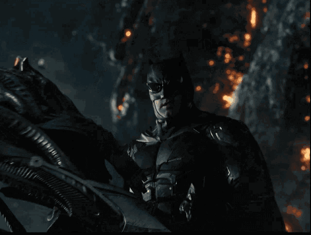 a man in a batman costume stands in front of a fire