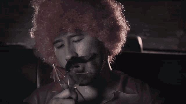 a man wearing a pink afro wig and a mustache drinks from a martini glass