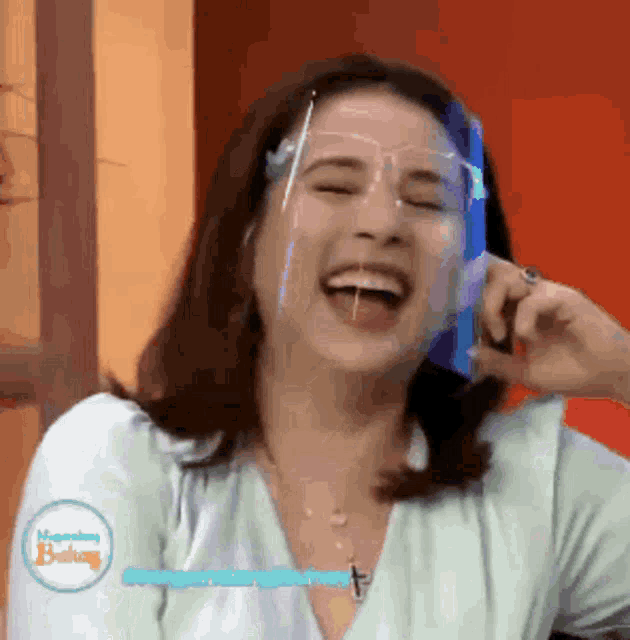 a woman wearing a face shield is laughing on a cell phone .