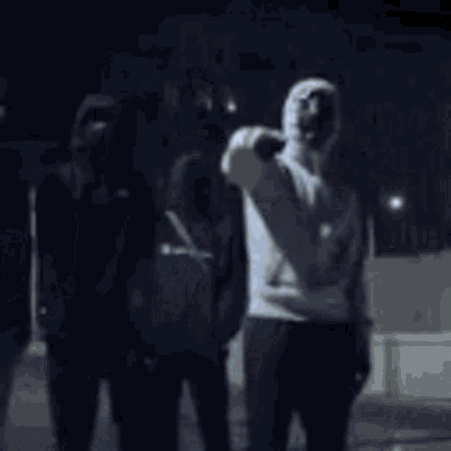 a man in a white hoodie is standing in a dark room with other people .