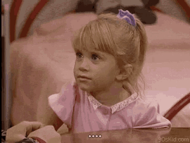 a little girl in a pink shirt is sitting at a table with a person .