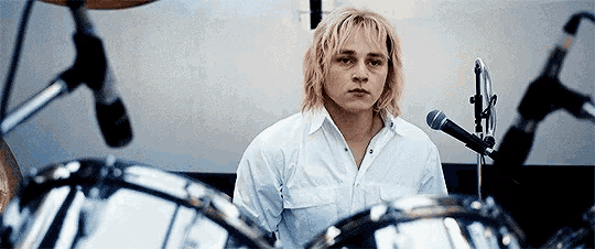 a man in a white shirt is playing drums in front of microphones