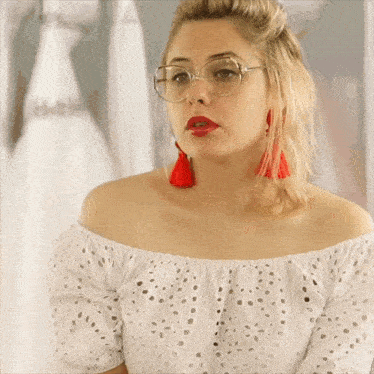 a woman wearing glasses and red tassel earrings looks at the camera
