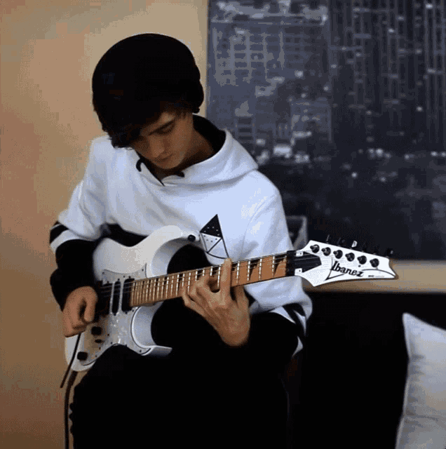 a young man is playing a white ibanez electric guitar