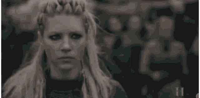 a woman with blonde hair and braided hair is standing in front of a crowd of people .