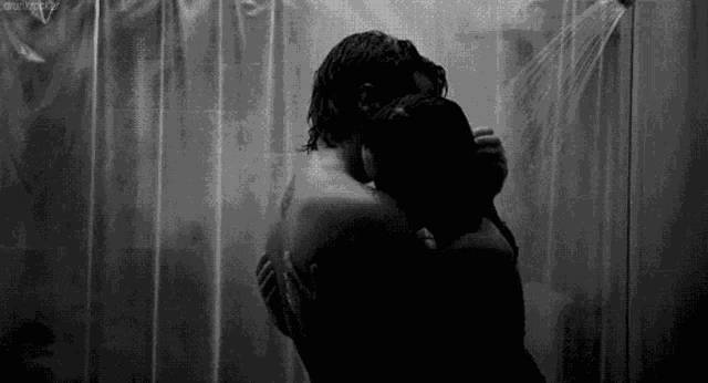 a man and a woman are hugging in a shower in a black and white photo .