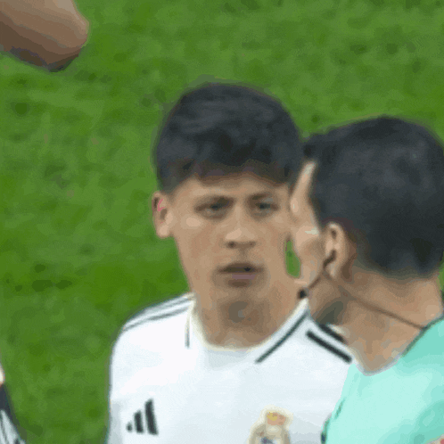 a soccer player wearing a white adidas jersey is talking to an umpire